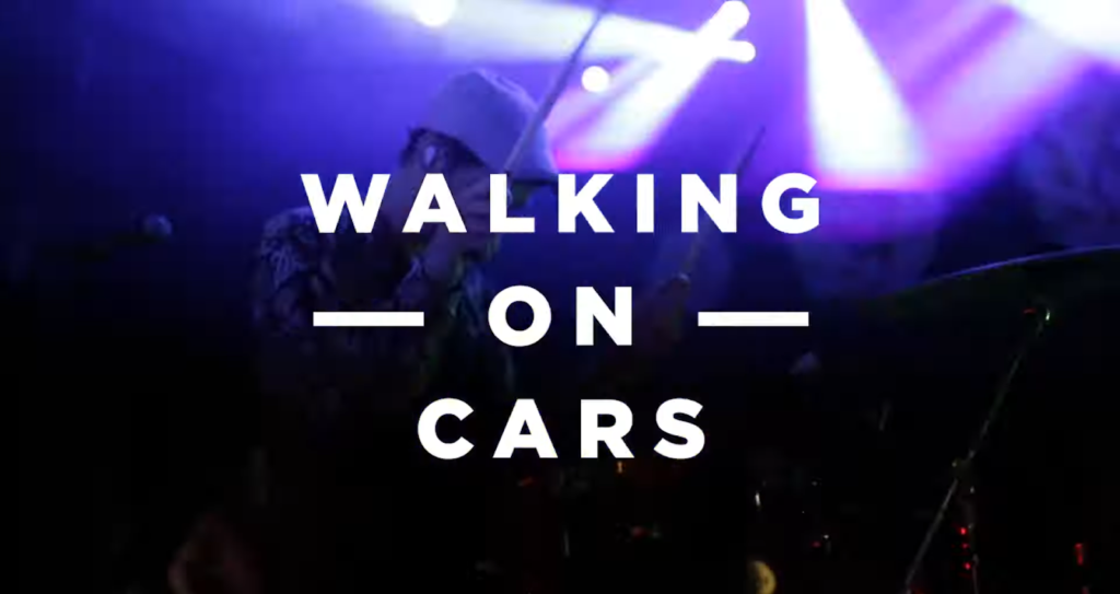 "WALKING ON CARS" on a dark purple background, the drummer behind